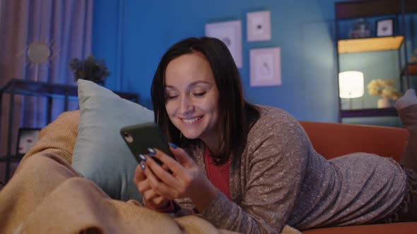 Woman Lying on Sofa at Home Using Mobile Phone Communicating in Social Network or Online Shopping