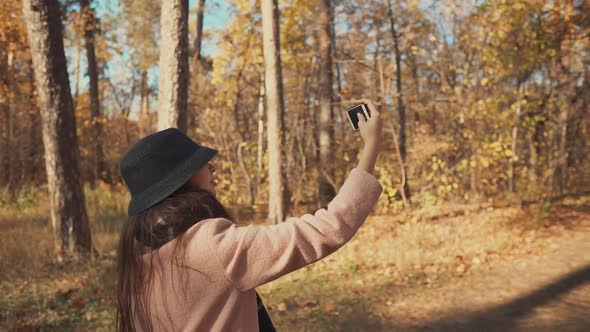 Young Blogger Girl Is Filming Herself By Phone on Walk in Autumn Forest