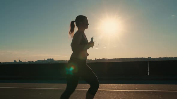 Silhouette of a Woman Jogging on a Road at Sunset