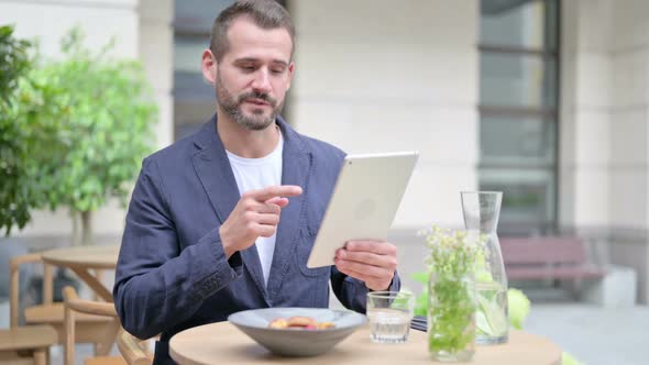 Man Making Video Call on Tablet Sitting in Outdoor Cafe