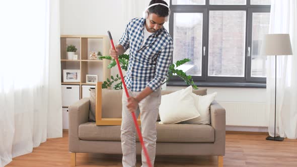 Man in Headphones with Broom Cleaning at Home