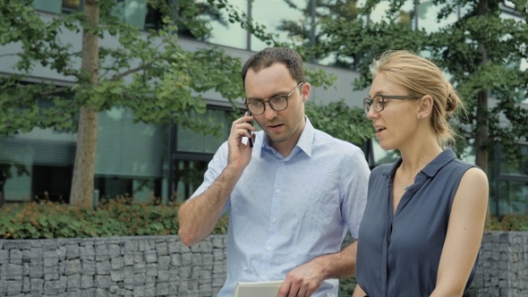 Business Partners Walking While One Making a Call on The Phone.