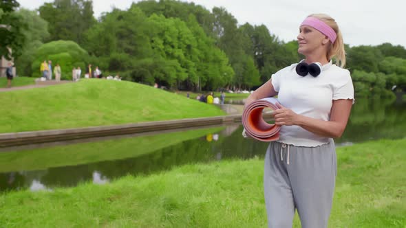 Mature Woman with Yoga Mat Standing in Summer Park and Relaxing After Exercise