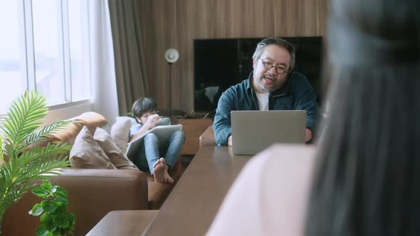 asian male dad using laptop and conversation on smartphone remotely distance working