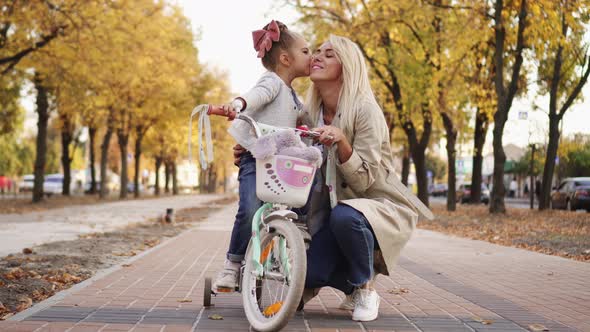 Little Girl Hugs and Kisses Her Mother While Walking in Park