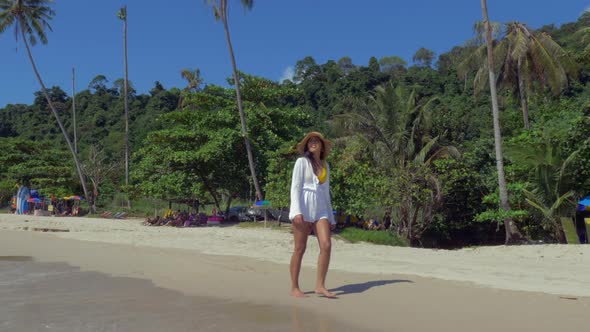 Slow motion shot of a woman in a white dress walking on a picturesque beach