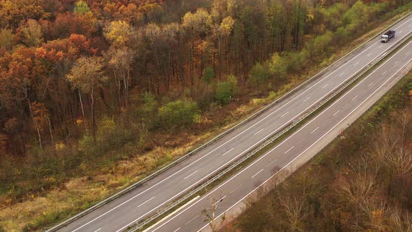 Trucks and Cars Drive on Freeway in Fall Forest - Tilt and Pan Shot 