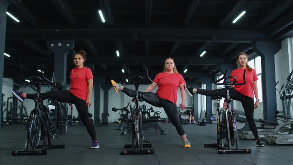 Healthy Caucasian Group of Women Exercising Stretching on Stationary Cycling Machine Bike in Gym