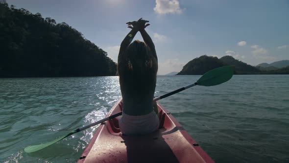 Silhouette of Woman Tourist Raising Hands While Sailing in Canoe Along Sea Bay Water to Distant