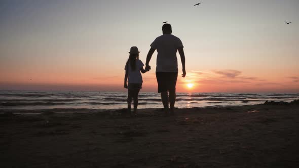 Silhouettes Father and Daughter Play on the Beach at Sunset. Concept of Friendly Family, Travel