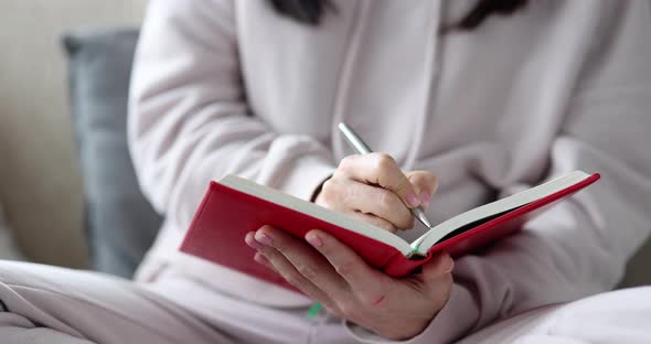 Woman Writer Writes Notes in Diary While Sitting on Sofa