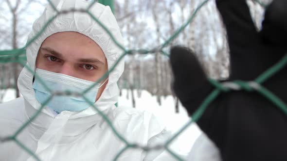 A Masked Man is Holding on to a Metal Mesh with His Hand