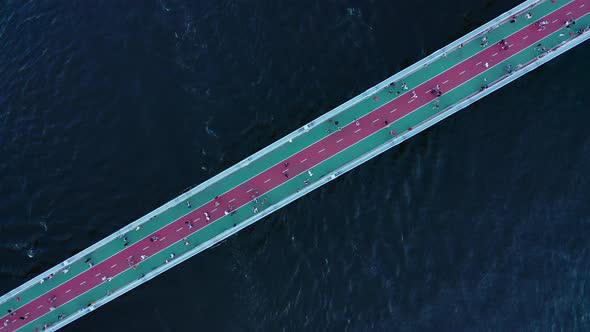 The Movement of People on a Footbridge Over a Large River with Dark Blue Water  Top Down Shot