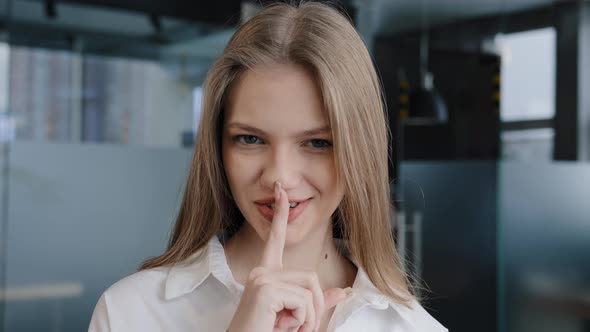 Closeup Young Caucasian Woman Smiling Standing Indoors Showing Silence Sign Looking at Camera