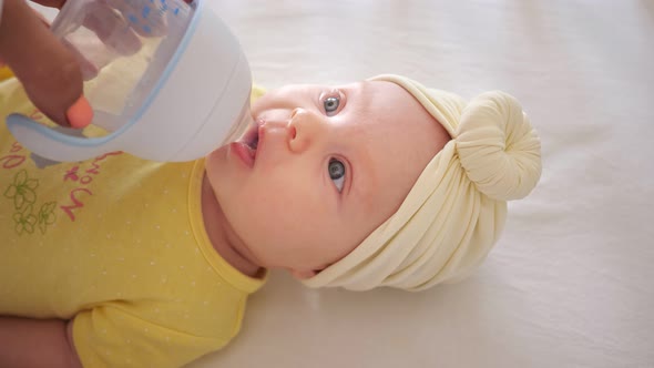 Mother Waters Curious Baby Girl From Bottle with Teat