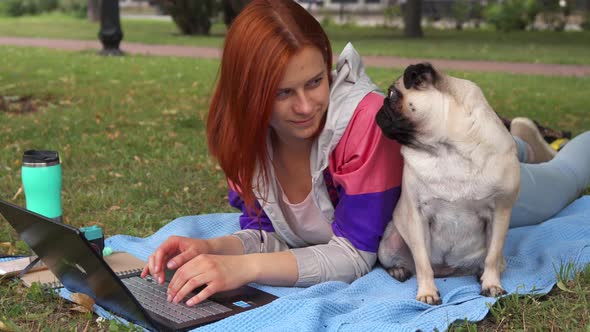 Girl Laying and Typing on Laptop on a Lawn with Her Pug Around