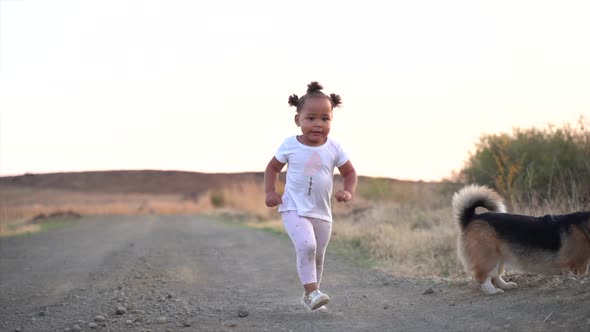 Small South African girl running with a dog on a grey gravel road in a country winter landscape at d