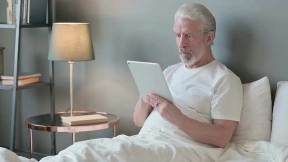 Old Man Reacting to Loss on Tablet in Bed