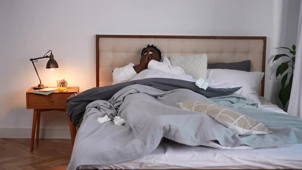 Wide Shot Exhausted African American Ill Man Lying in Bed at Home with Runny Nose