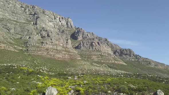 Aerial lower angle scenic drone flight view of Table Mountain in late afternoon sun against blue sky