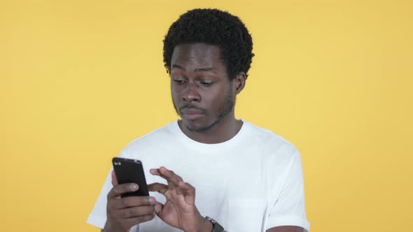 African Man Excited for Success on Smartphone, Yellow Background