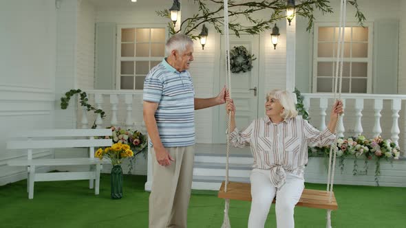 Senior Couple Together in Front Yard at Home. Man Swinging Woman. Happy Elderly Pensioners Family