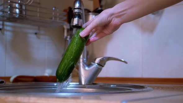 Female Washing Green Cucumbers with Running Water From a Tap in a Modern Kitchen