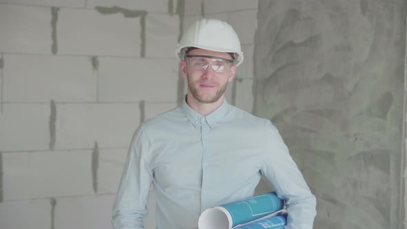 Young engineer-architect with  blueprints looks at the camera 