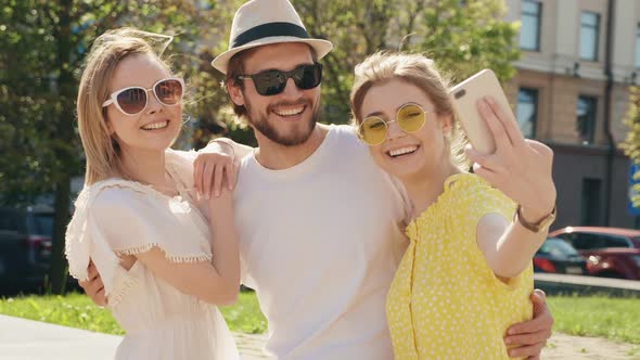 Group of young three stylish friends posing in the street. Fashion man and two cute girls outdoors