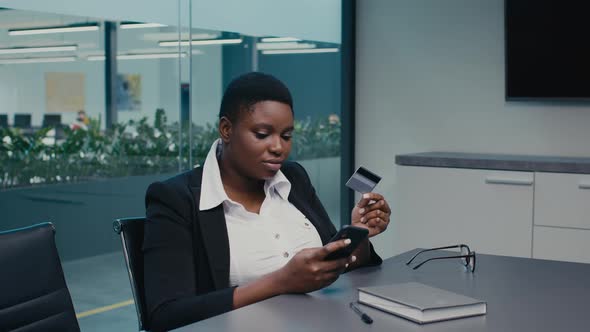 Young Black Businesswoman Using Credit Card And Smartphone At Workplace In Office