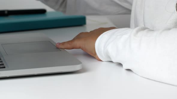 A child girl on distance learning sits in front of a laptop and does homework.