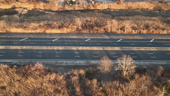 An aerial view of a salt marsh next to a multilane road with a few cars driving by, shot on a sunny