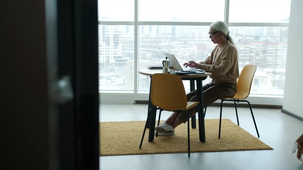 Serious Businesswoman Working From Home Using Laptop Typing at Kitchen Table