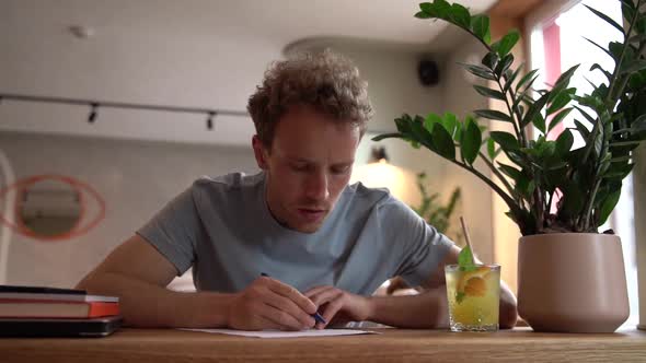 Attractive, young man writes something while sitting at a table in a cozy cafe.