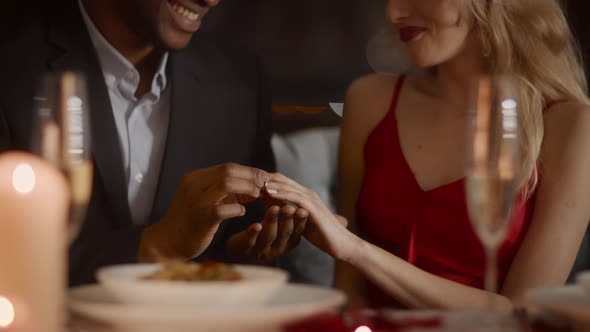 Black Man Proposing To Woman Putting On Ring In Restaurant