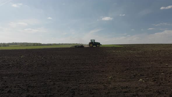 Agricultural green big tractor plows in the field.