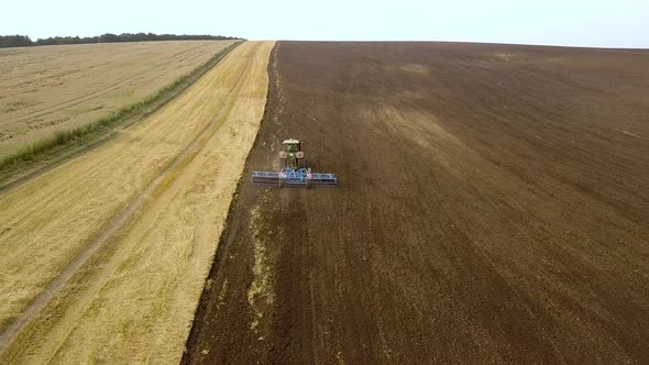 Aerial footage of a tractor plowing black agriculture farm field after harvesting in autumn