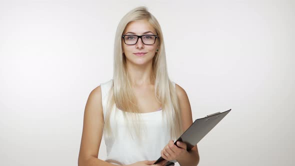 Cute Young Blond Businesswoman Wearing Glasses Posing at Camera Smiling Holding Clipboard Over White