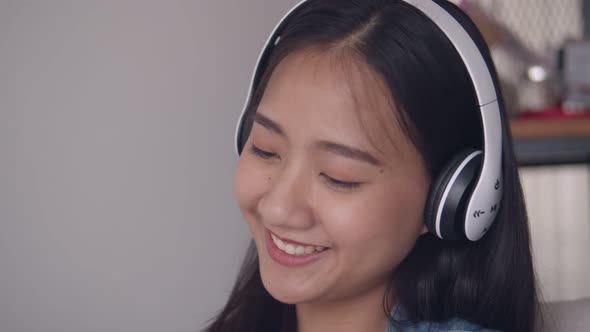 Asian woman listening to music on headphones While sitting sofa in the living room at home.