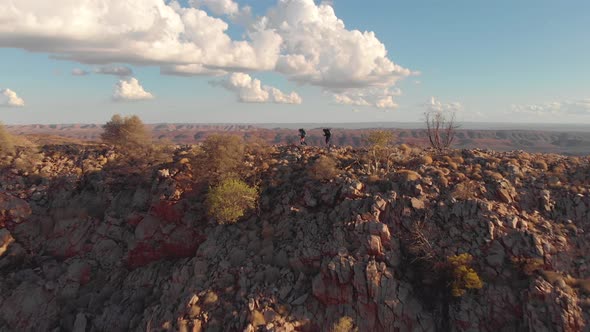 Aerial pan, hikers on rocky mountain ridge, blue sky and white clouds