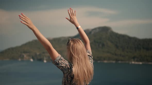 Hair Flying On Sea Breeze Wind. Girl Sitting On Cliff And Looks At The Sea. Woman Sitting On Rock.