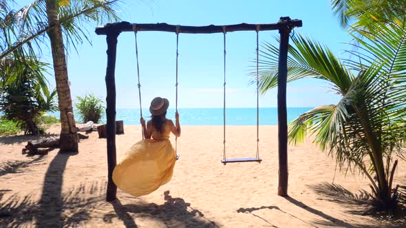 Woman Tourist Swinging on Swing on Sandy Beach with Palm Trees and Blue Sea