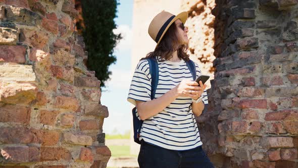 A Young Woman Uses Her Phone While Standing at the Old Ruined Fortress