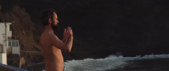 Topless man meditating and doing qigong in front of the sea