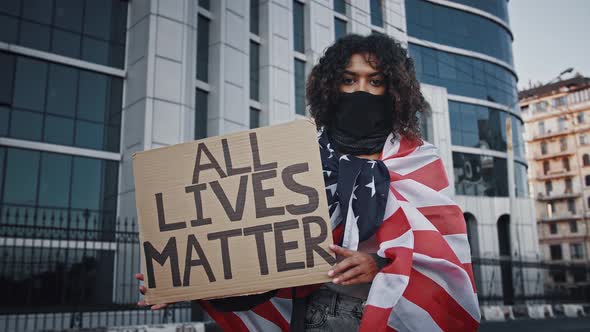 Darkskinned Protester Woman in Black Bandana on Face Wrapped in Flag of USA