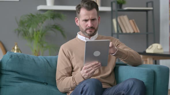 Man Having Loss on Tablet on Sofa