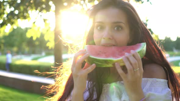 Young Beautiful Woman Eating Ripe Watermelon in the Park on a Summer Day