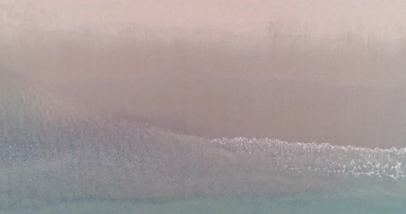 Static top down view of tropical beach, foamy ocean waves washing sand. Waves hitting sand beach