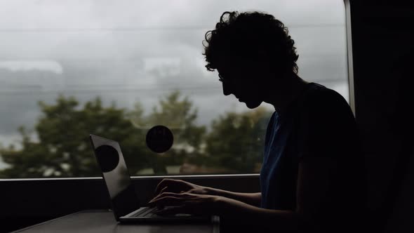 Silhouette of a Woman in Glasses Working on a Laptop While Going By Train