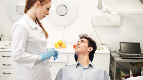 Young Attractive Female Dentist Talking with Man Sitting in Dental Chair About Teeth Problems